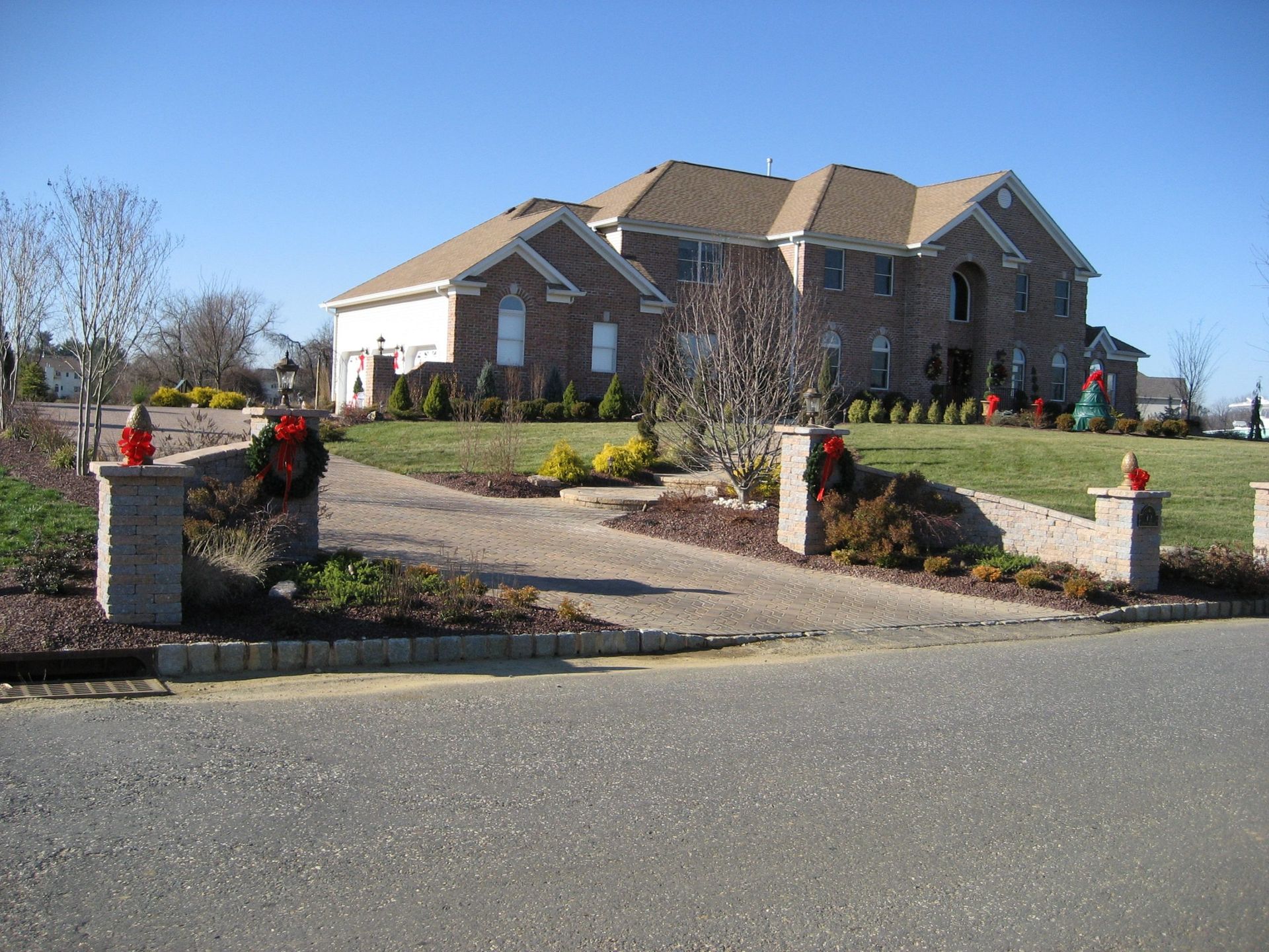 Brick house with driveway, columns with wreaths, and lawn on a sunny day.
