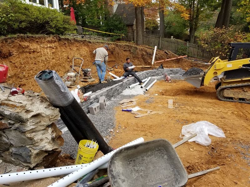 Construction site with workers, retaining wall, bulldozer, and materials.