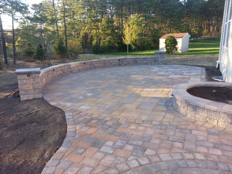 Brick patio with curved retaining wall and a planting bed; trees in the background.