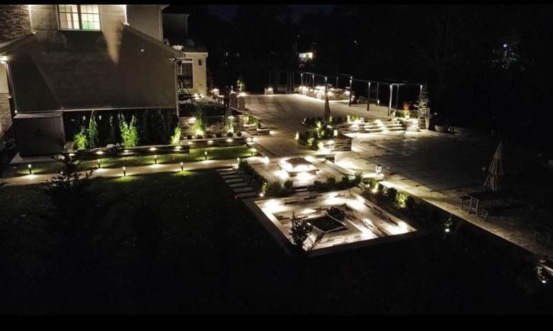 Overhead view of a square, tiered patio with a central fire pit, surrounded by gravel and grass.