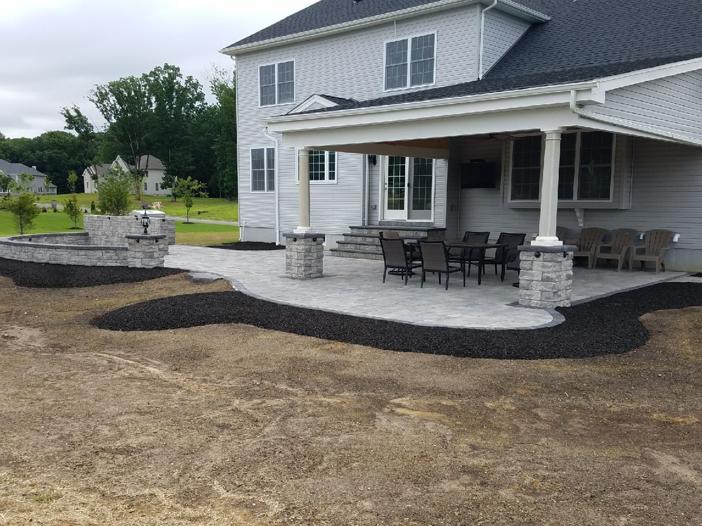 Backyard patio with seating, landscaping, and a covered porch attached to a two-story house.