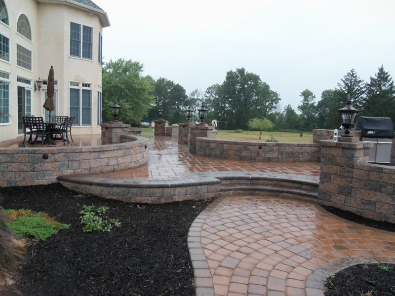 Stone patio with curved walls, steps, and circular brick path, next to a large house.