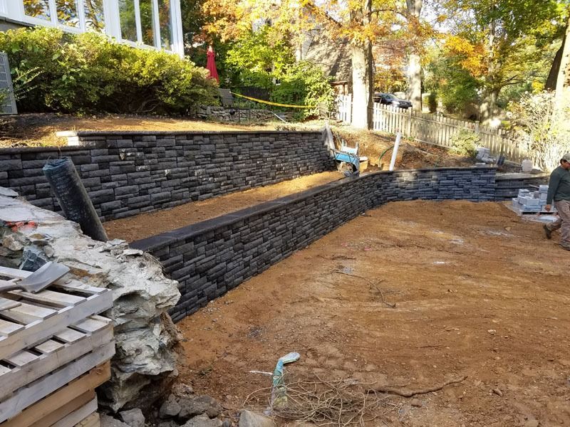 Construction site with dark stone retaining walls and dirt, likely for landscaping.