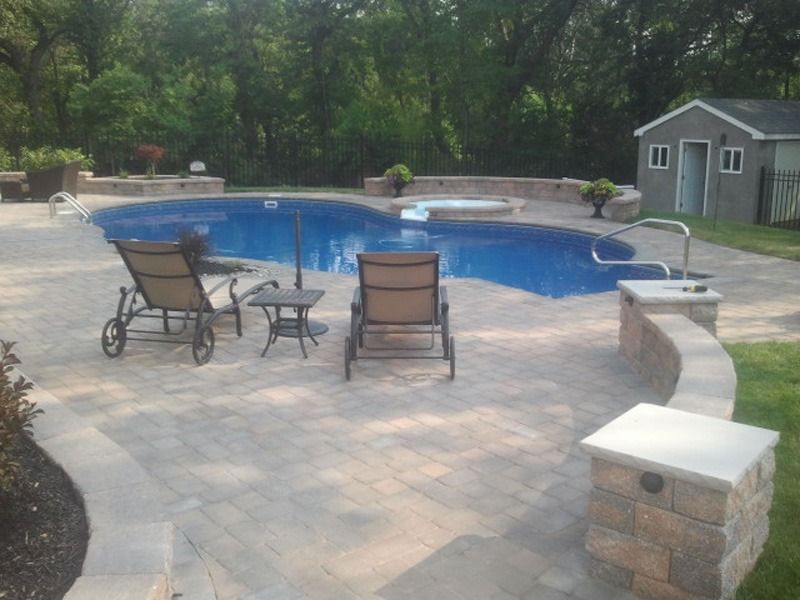 Swimming pool with patio, lounge chairs, and spa in a backyard setting.