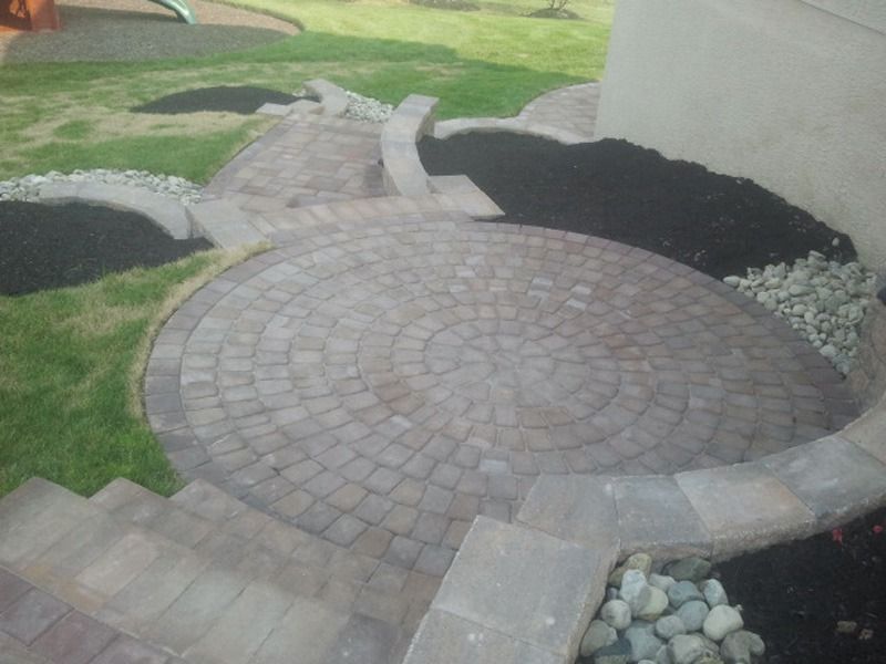 Circular brick patio with steps and surrounding garden beds filled with mulch and rocks.