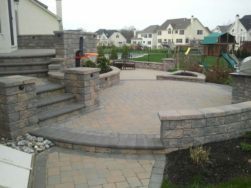 Brick patio with steps, retaining walls, and fire pit in a residential backyard.