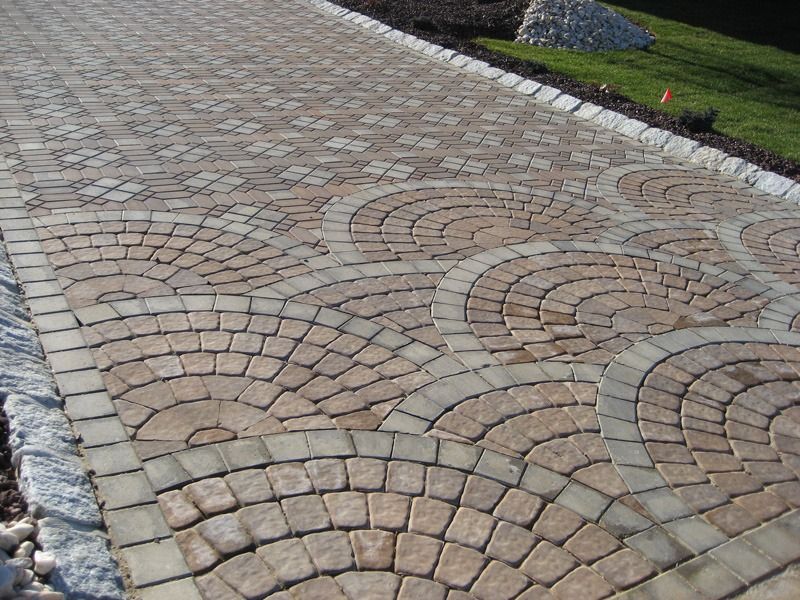 Brick paved driveway with a fan-shaped design, bordered by stone and grass.
