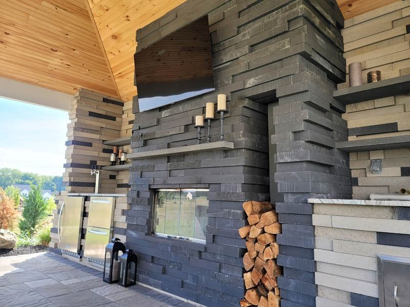 Outdoor stone fireplace with a stacked wood holder, a TV, and shelves.