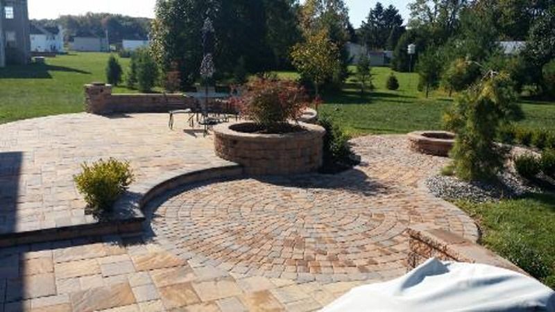 Brick patio with built-in planters and fire pit in a backyard with green grass.