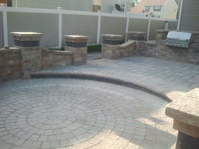 Brick patio with built-in grill and decorative pillars, enclosed by a fence.