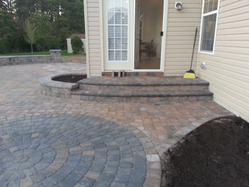 Brick patio with steps leading to a sliding door; a circular pattern and planting bed are also visible.