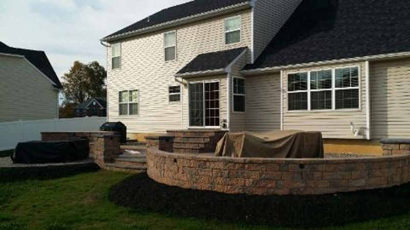 Backyard patio with tiered brick retaining walls, leading to a house with a sliding glass door.