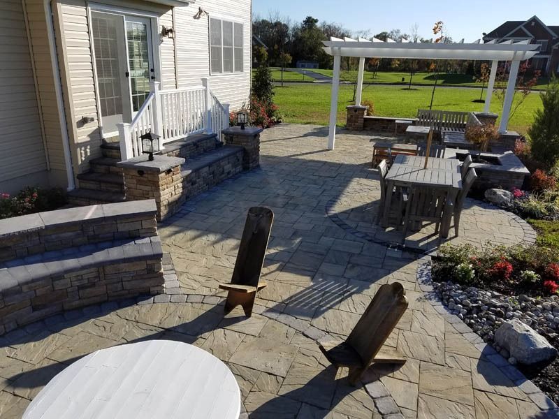 Patio with stone pavers, seating, steps, a pergola, and garden beds.