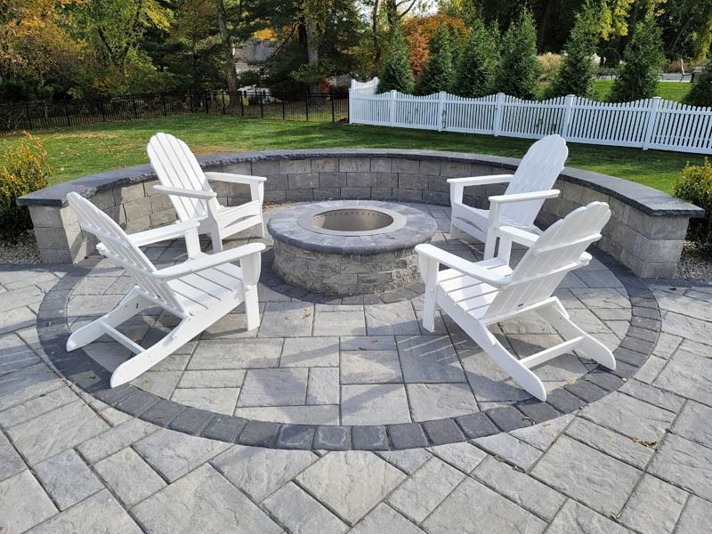 Four white Adirondack chairs around a stone fire pit on a paved patio.