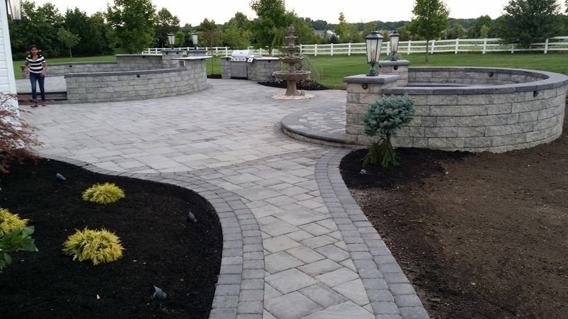 Brick patio with stone walls, walkway, and landscaping in a yard.