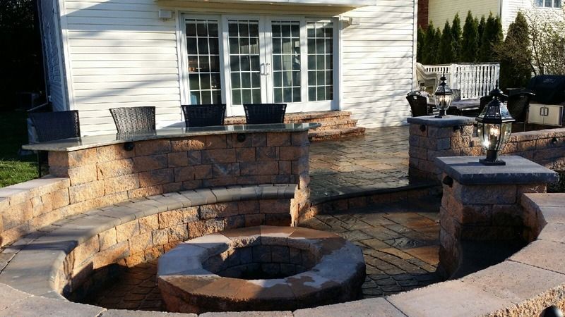 Stone patio with built-in seating, a fire pit, and a bar area with windows in the background.