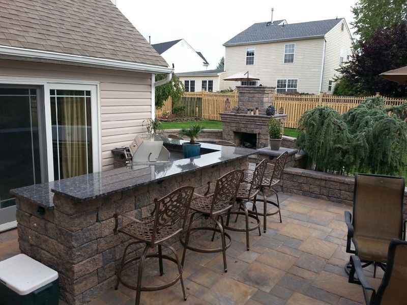 Outdoor bar with granite countertop and bar stools, brick facade, adjacent to a patio and backyard with a fireplace.