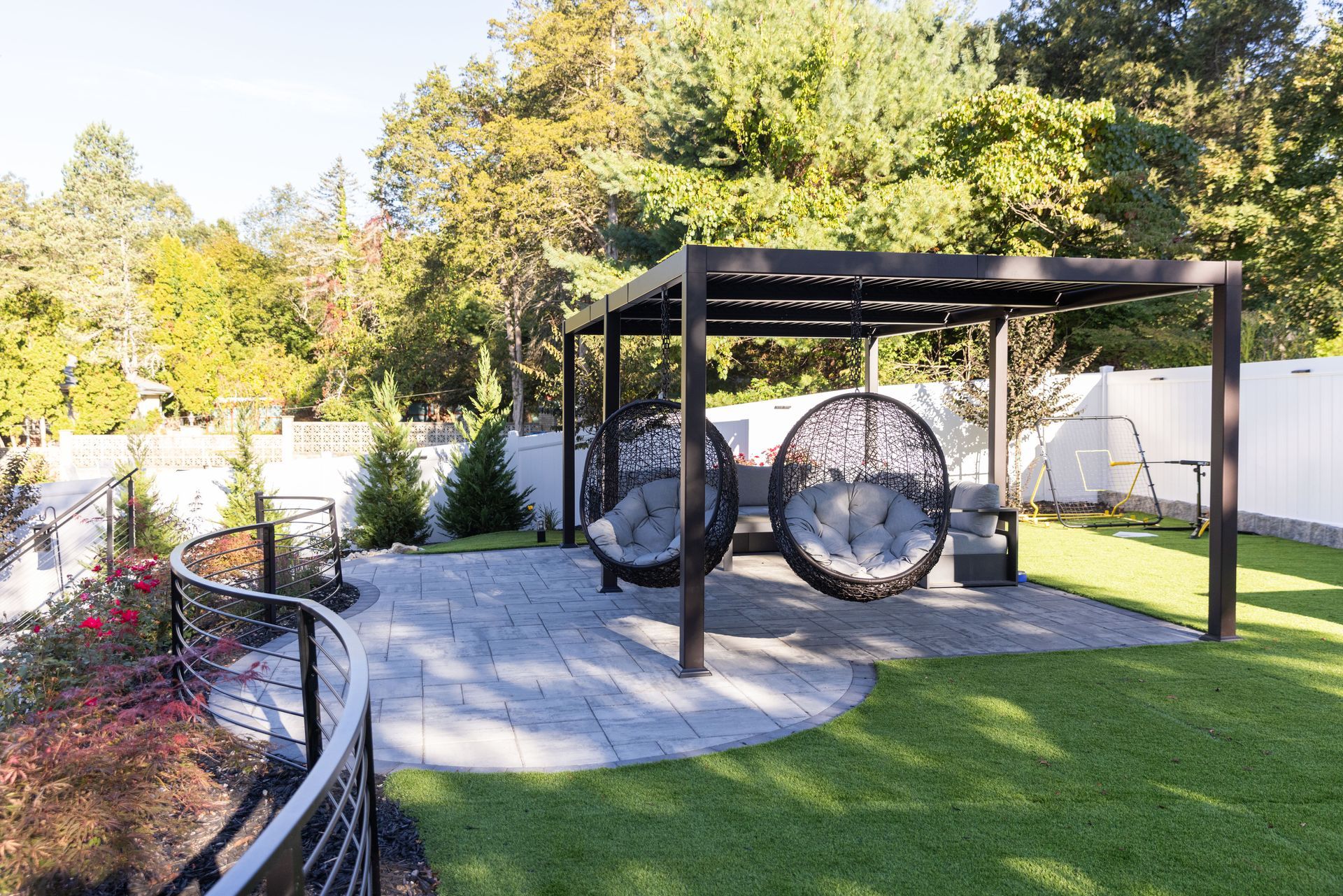 Outdoor patio with gray paving, pergola, hanging chairs, and green lawn.