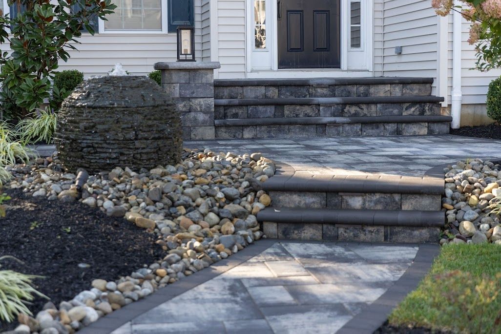 Gray stone steps and walkway leading to a house entrance, with rock landscaping and a small water feature.