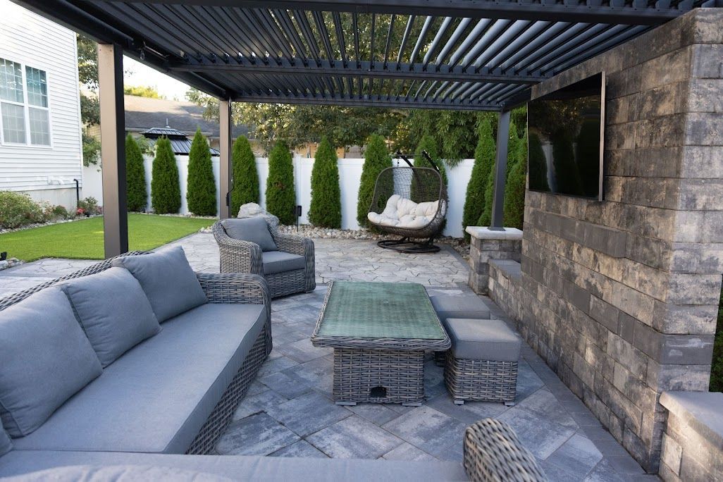 Patio with gray furniture, a pergola, and a built-in TV on a stone wall.