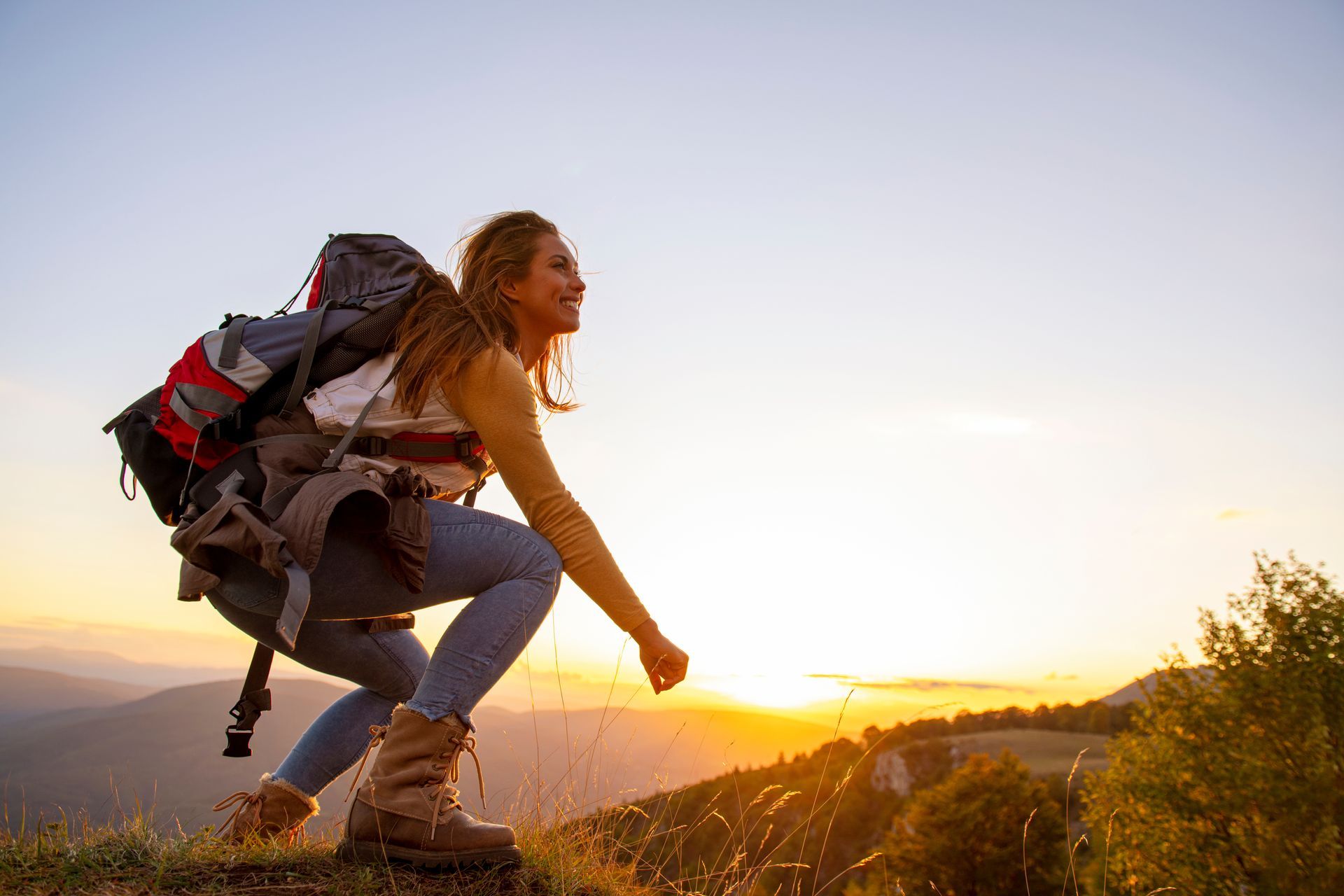 Woman hiker with backpack at sunrise, looking joyful on a mountain.
