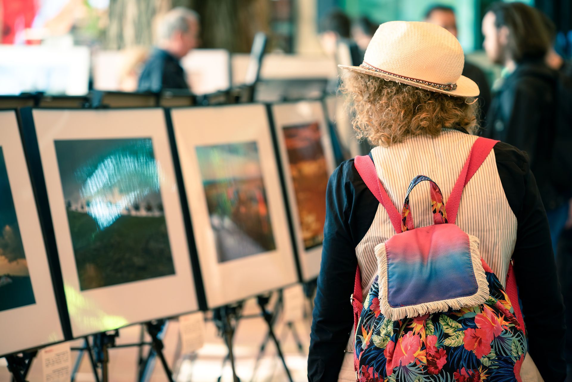 Woman with backpack looks at framed artwork at an outdoor art fair.