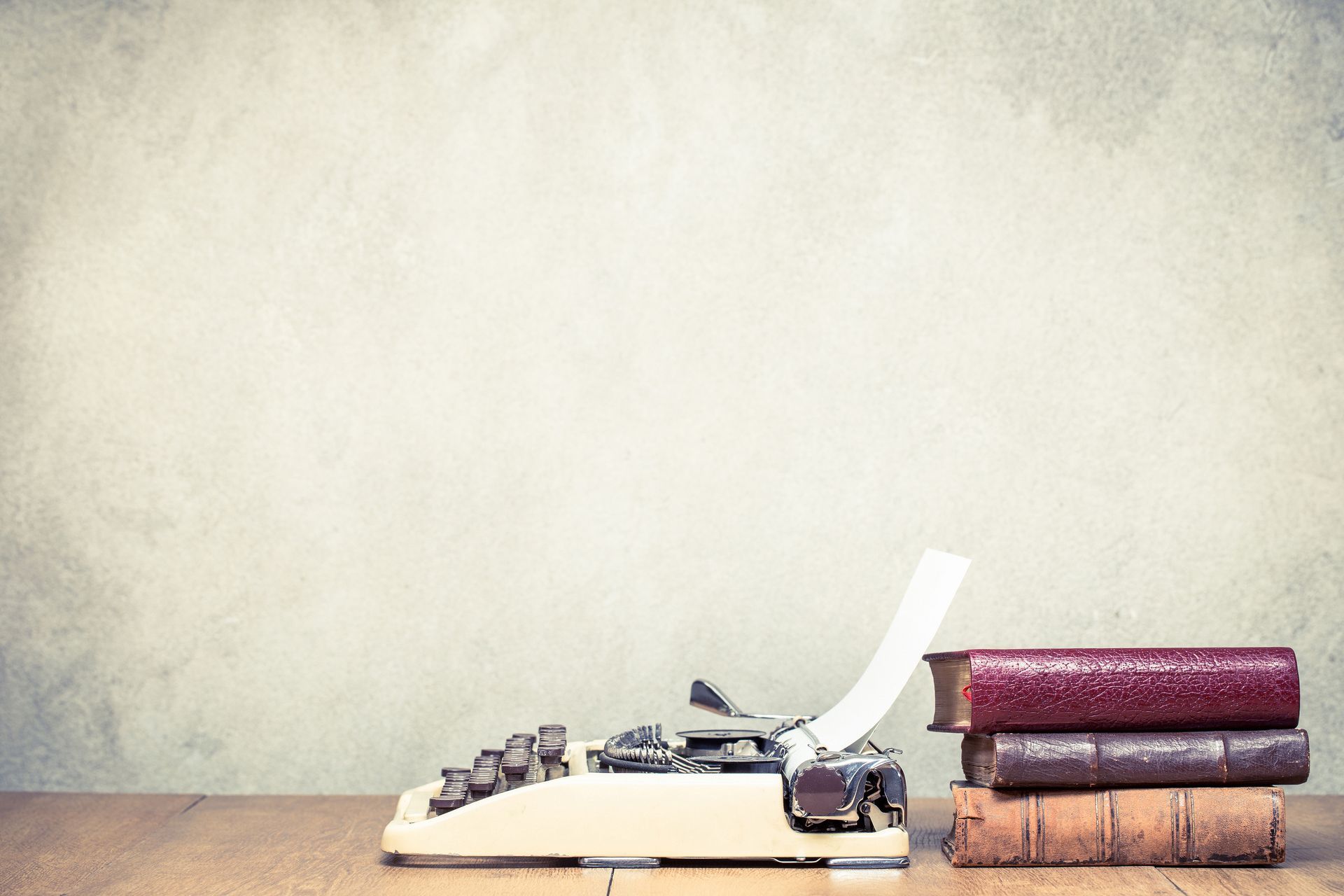 Vintage typewriter with paper, beside a stack of books on a wooden table.