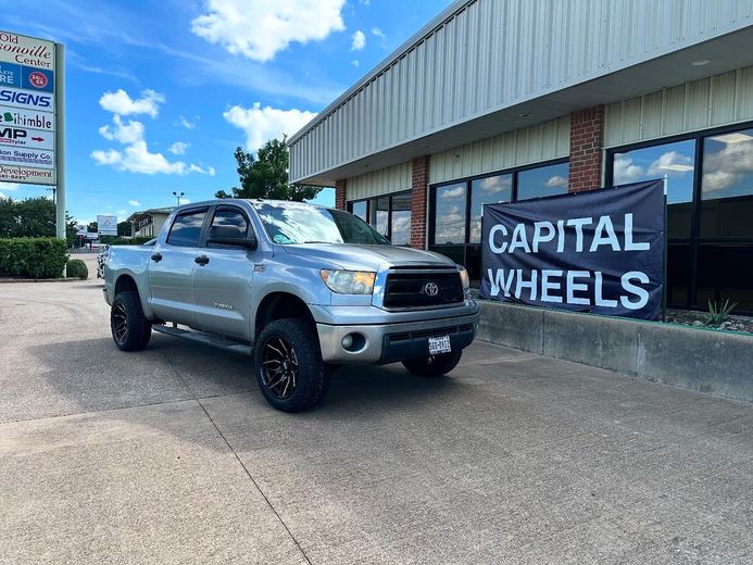 A silver truck is parked in front of a building with a sign that says capital wheels.