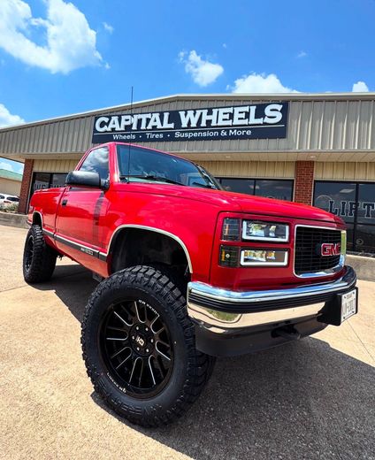 A silver truck is parked in front of a building with a sign that says capital wheels.