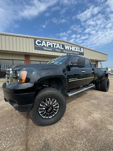 Black dually pickup truck in front of a Capital Wheels store on a sunny day.