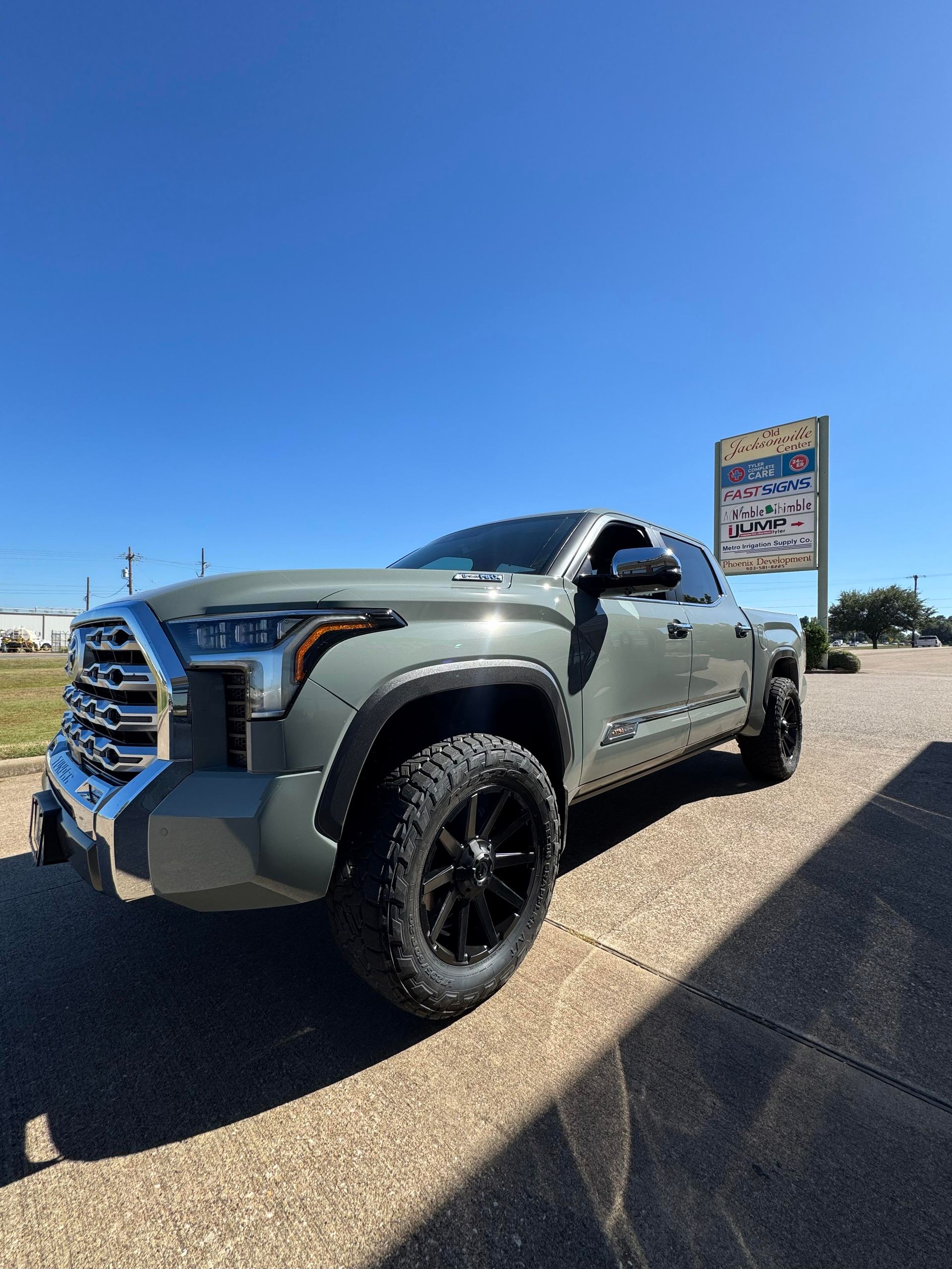 Gray Toyota truck with black wheels, parked on a paved area with a clear blue sky.