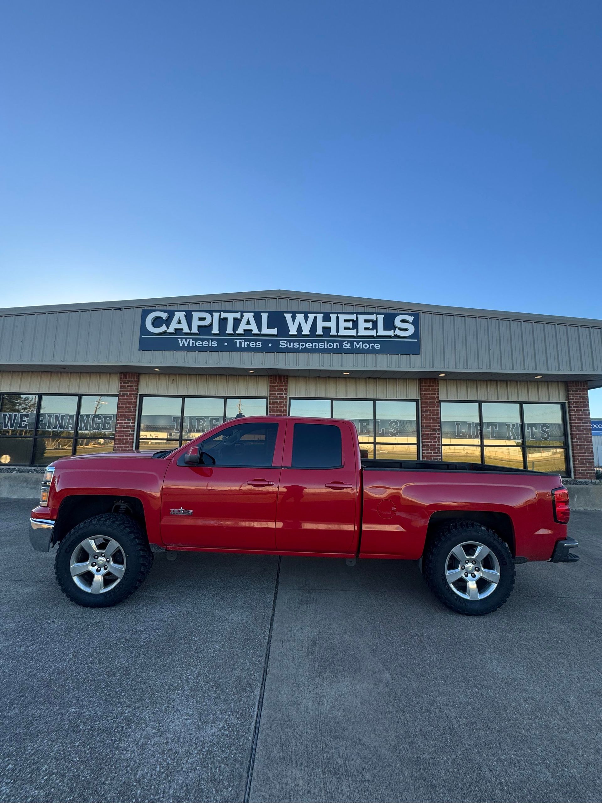 Red pickup truck parked in front of Capital Wheels shop under a blue sky.