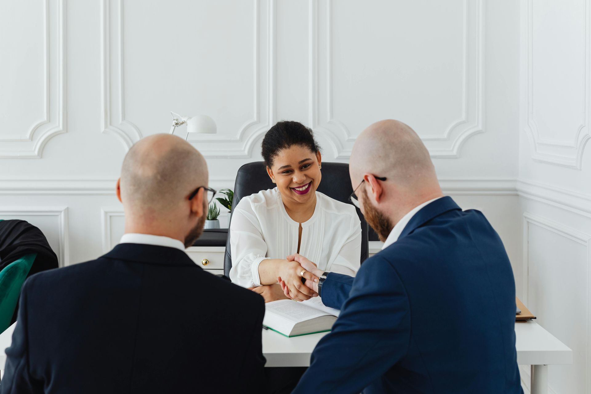 A woman is shaking hands with two men while sitting at a table.