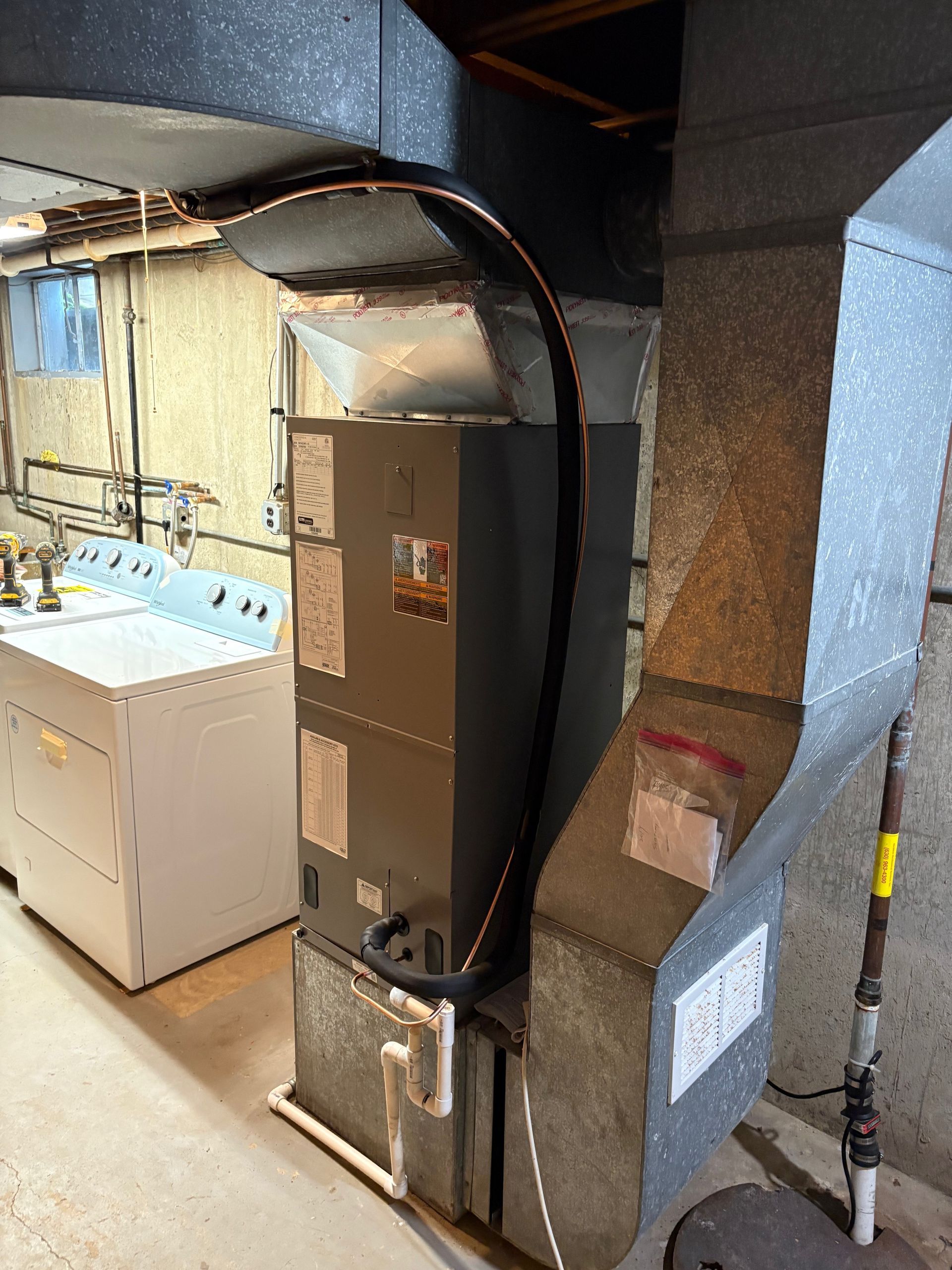 Furnace and ductwork in a basement laundry area, next to a washing machine.