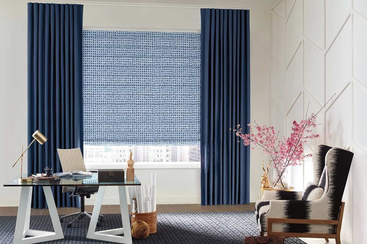 A home office decorated with blue Hunter Douglas Roman Shades and a branch of pink cherry blossoms near Kent, WA