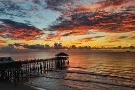 Cocoa Beach Pier at sunrise with surfers and oceanfront homes — best surf town and coastal living on