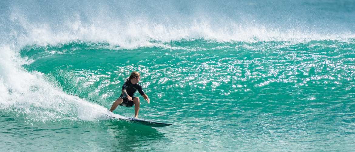 A surfer rides a wave at Cocoa Beach, Florida, with the iconic Cocoa Beach Pier and clear blue skies