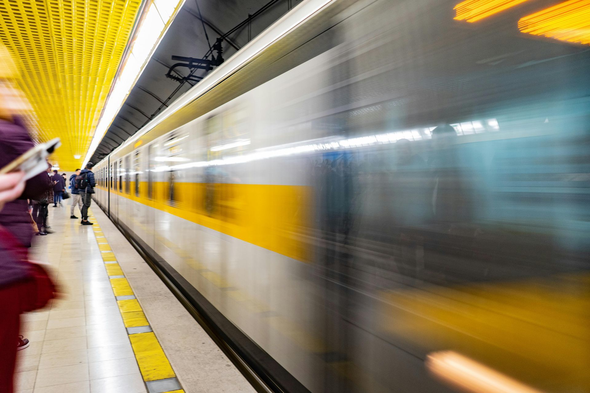 Train speeding past a subway platform, yellow accents, blurred motion.