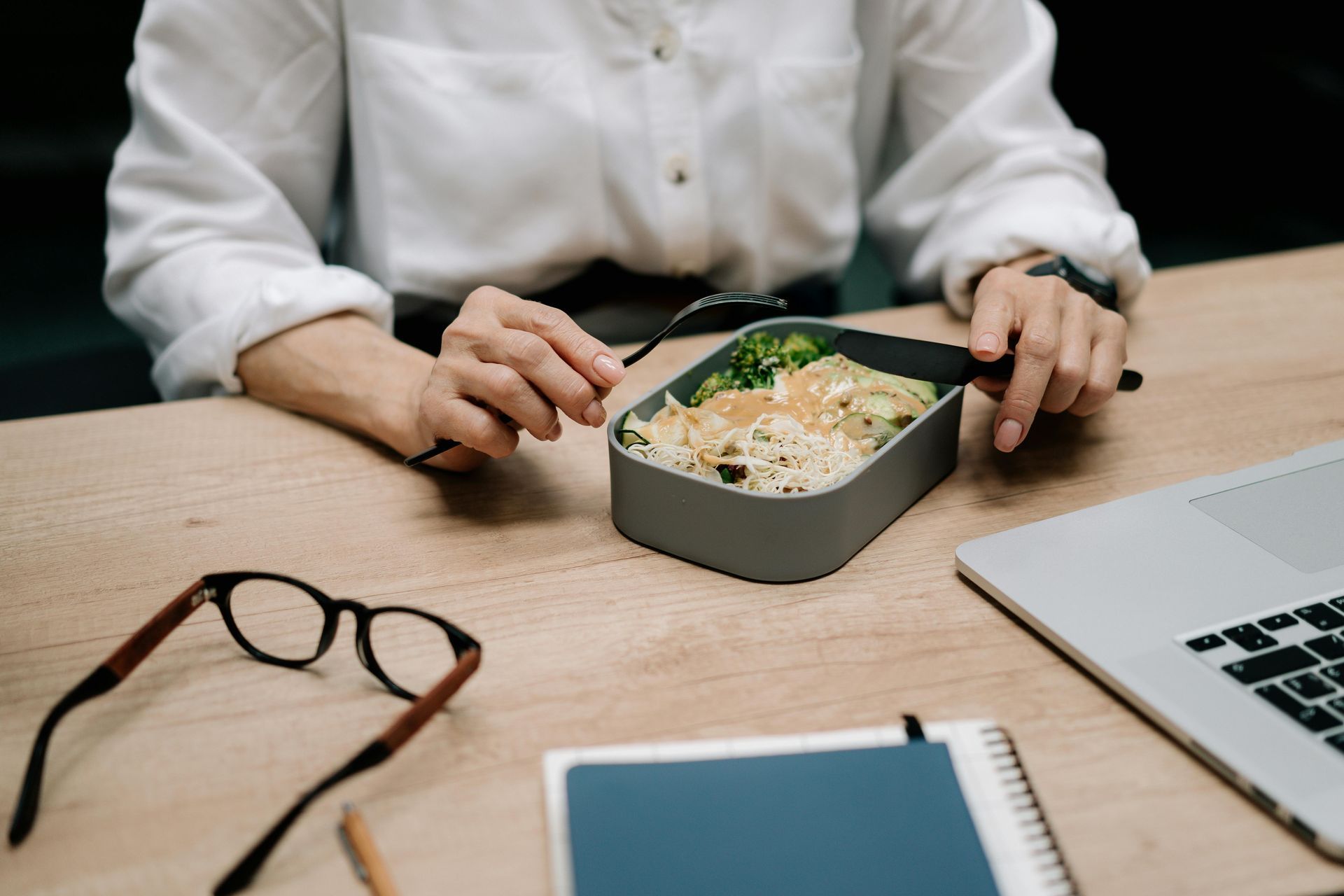 A woman is sitting at a desk eating a meal from a lunch box.
