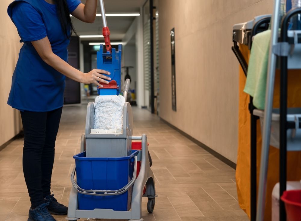 A woman is cleaning a hallway with a mop and bucket.
