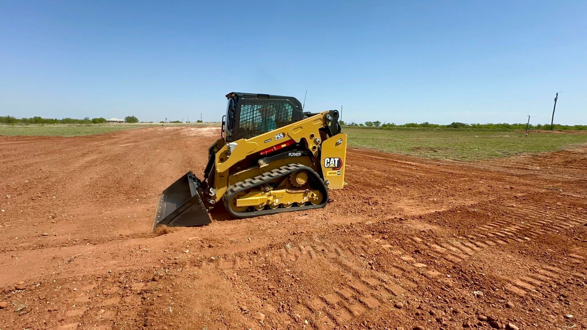 A yellow Caterpillar skid-steer loader with tracks moving soil on a construction site under a blue sky.