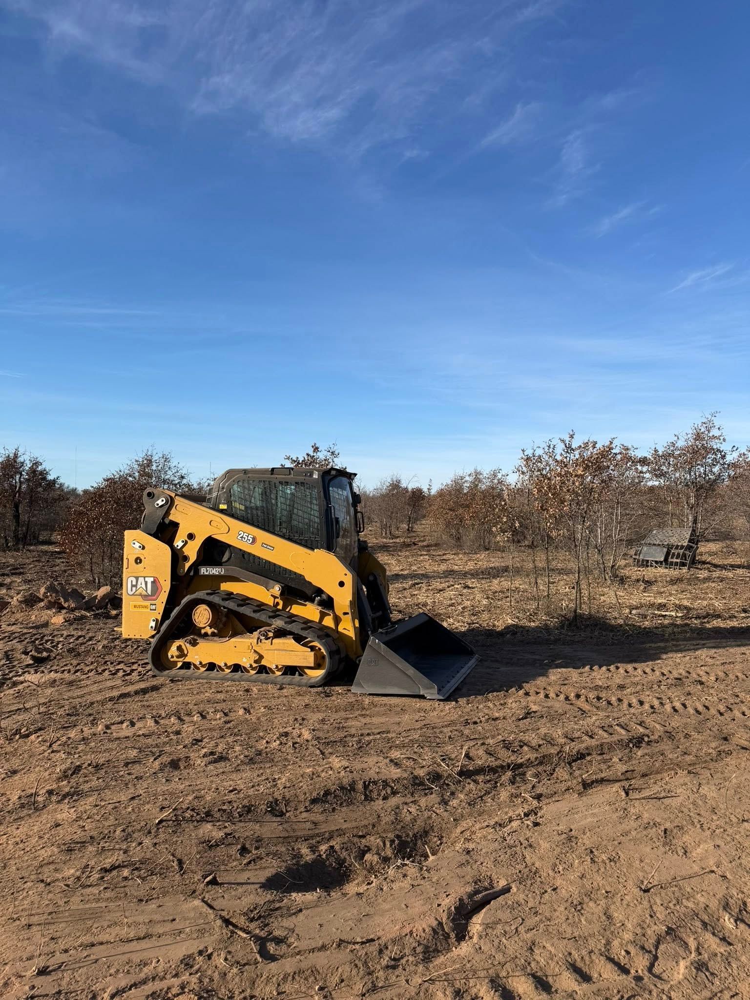 Yellow Caterpillar skid steer in a dirt field under a blue sky.