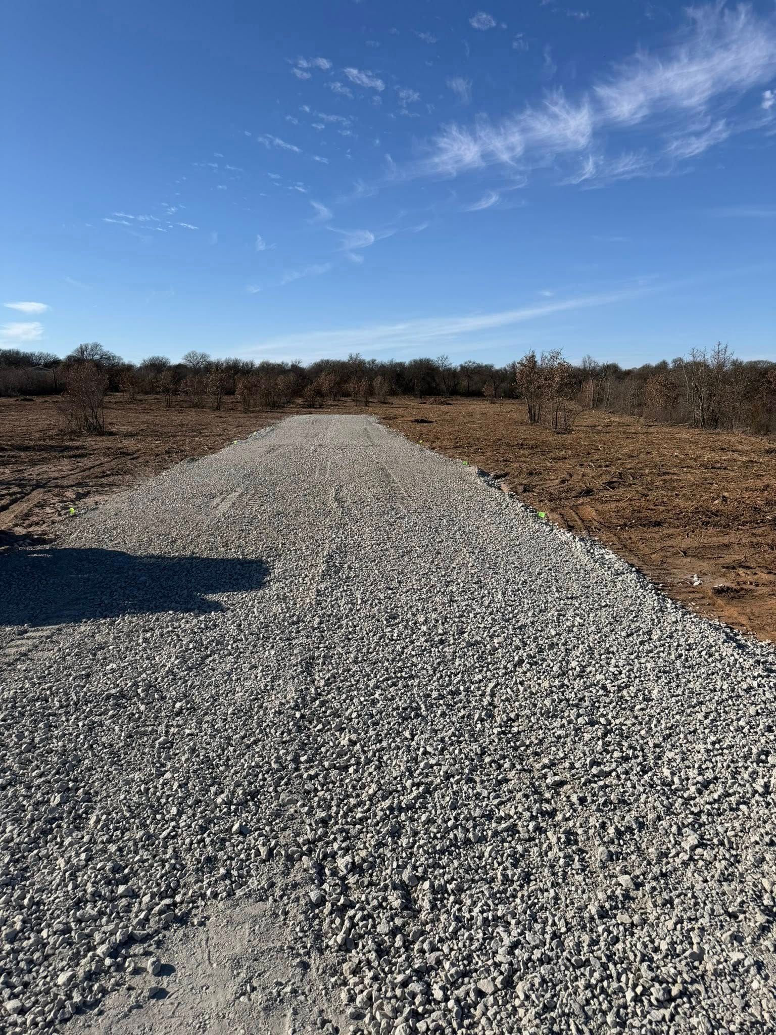 Gravel road in a field under a blue sky with scattered clouds.