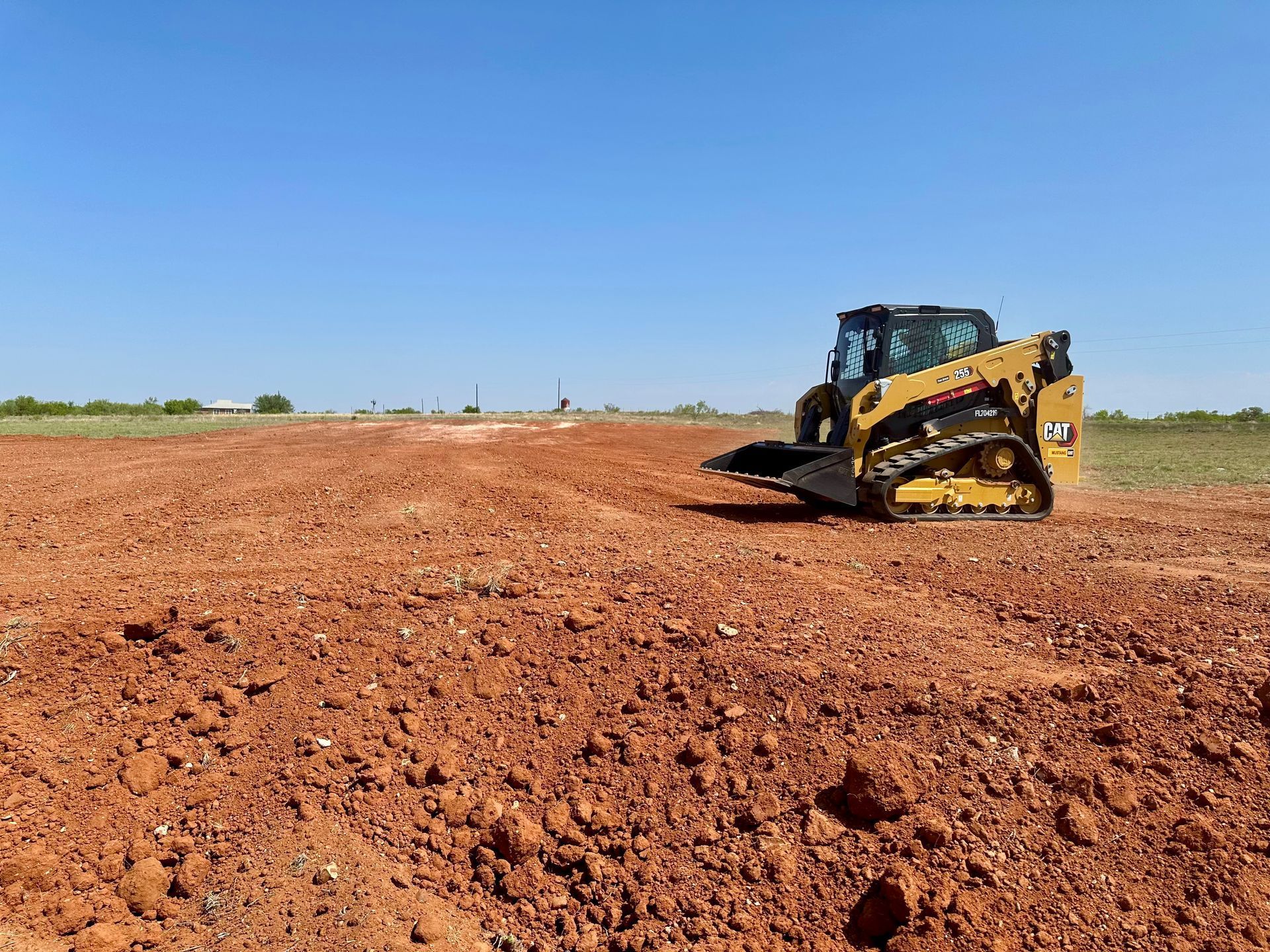 A yellow Caterpillar skid steer on a red dirt field under a blue sky.