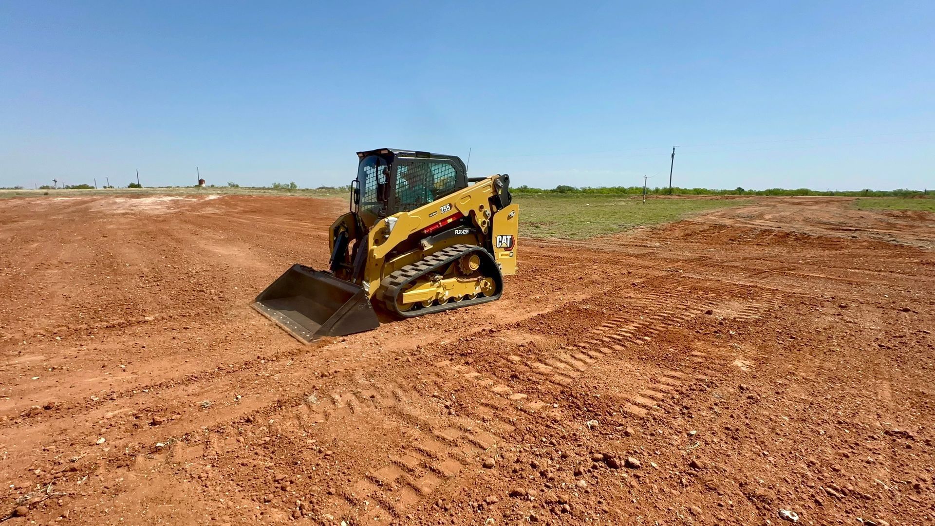 Yellow construction vehicle on tracks leveling dirt in a field under a blue sky.
