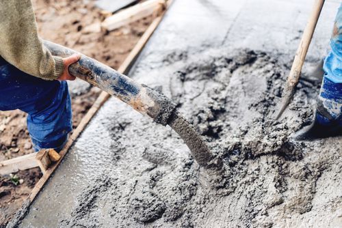 Workers pouring wet concrete into a form with a hose and smoothing it with a tool.