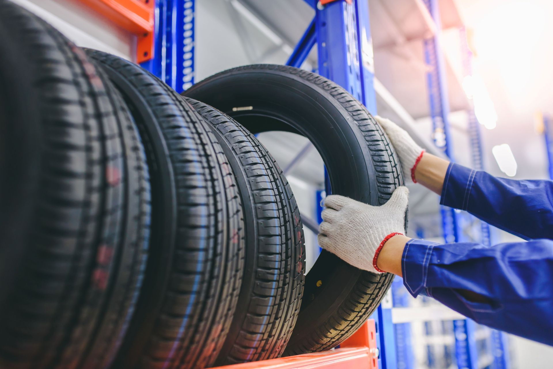 A worker is organizing car tires on a storage rack while wearing gloves.