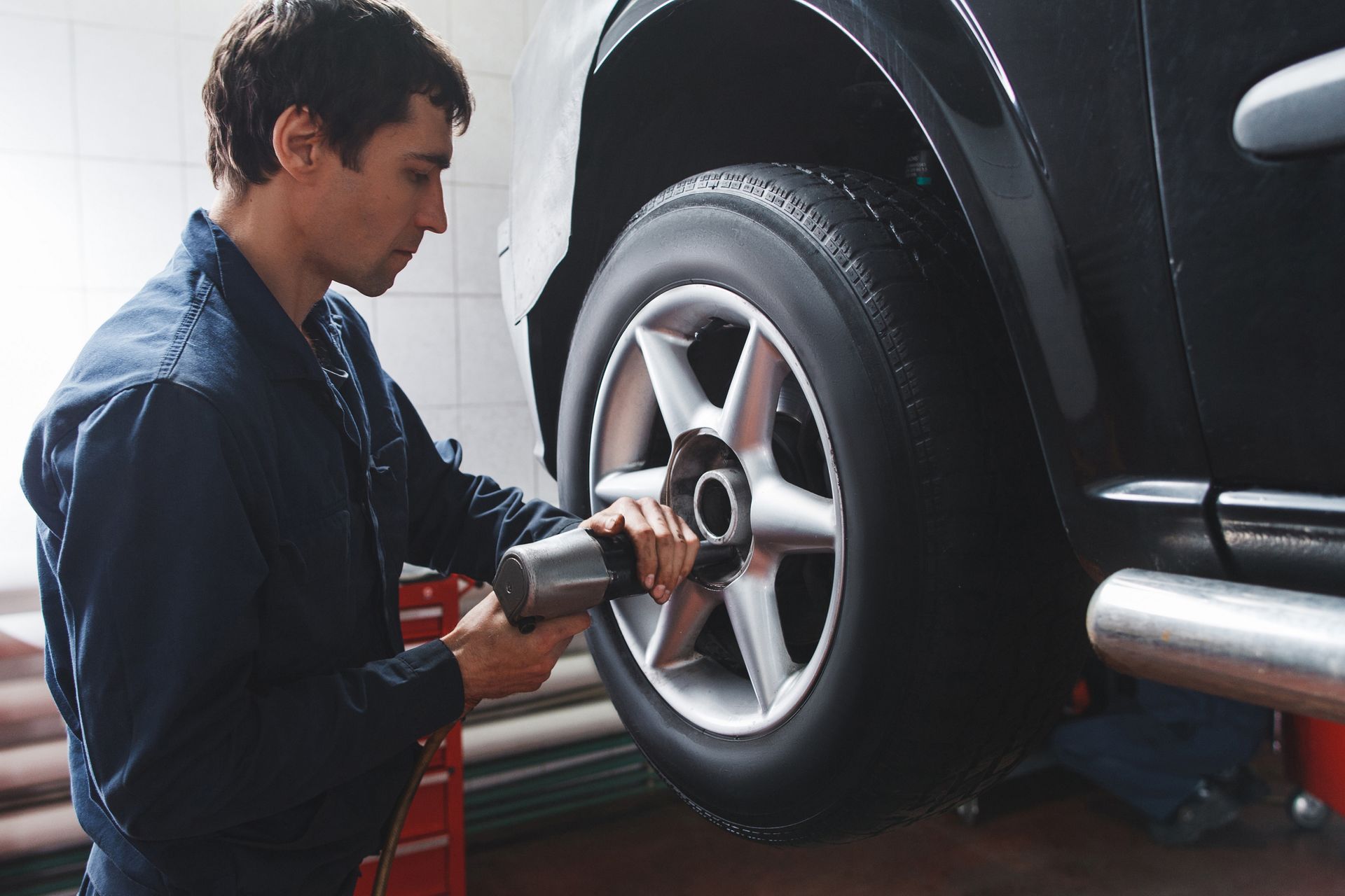 Mechanic tightening car wheel lug nuts with power tool in professional auto repair shop.