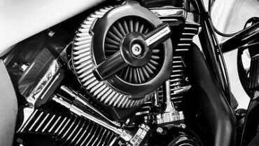 Détail moteur moto : filtre à air rond avec barres transversales, composants chromés, noir et blanc.