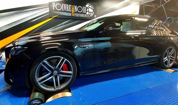 Berline Mercedes noire sur un banc d'essai dans un atelier de tuning, montrant sa roue et ses étriers de frein rouges.